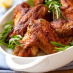 Crispy buffalo wings in a white platter garnished with fresh rosemary sprigs