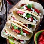 Shows a cutting board with five handmade tacos.