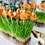 Creative display highlighting grilled shrimp skewers on a bed of wheatgrass tufts