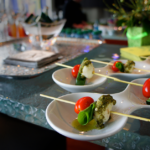 Fresh caprese skewers in circular white glass plates featuring fresh mozarella, pesto, basil, and baby tomato