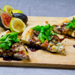 Shows a cutting board featuring three slices of fig pizza garnished with fresh basil and several cut figs as decoration.