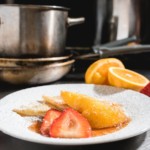 Close-up of crepes dusted with powdered sugar and topped with fresh strawberries