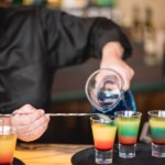 Layered cocktails being carefully poured to create red, green, and yellow color effects at the Quantum Kitchen even